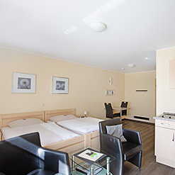 Doppelzimmer mit Betten, Sesseln und Küchenzeile